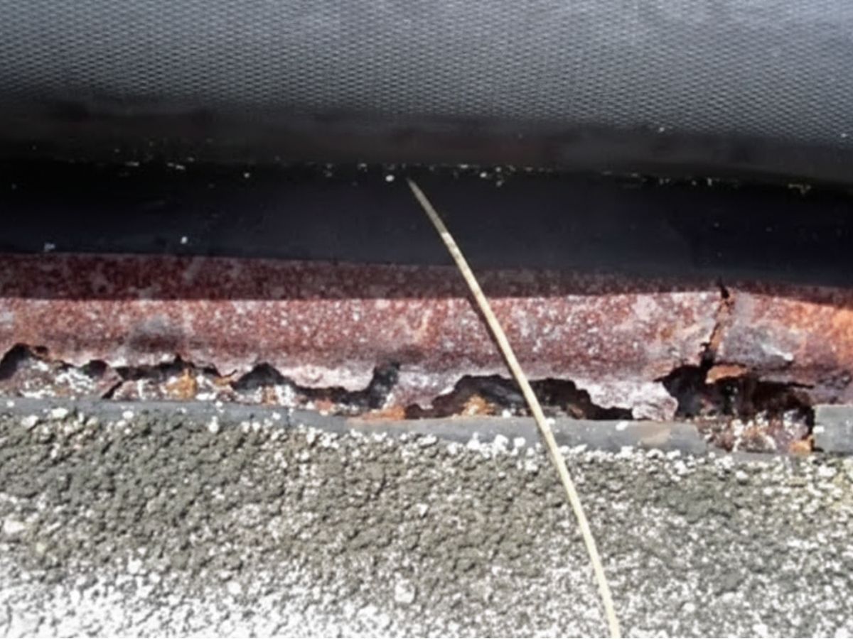 Corroded metal drip edge with rust deterioration beneath roof shingles