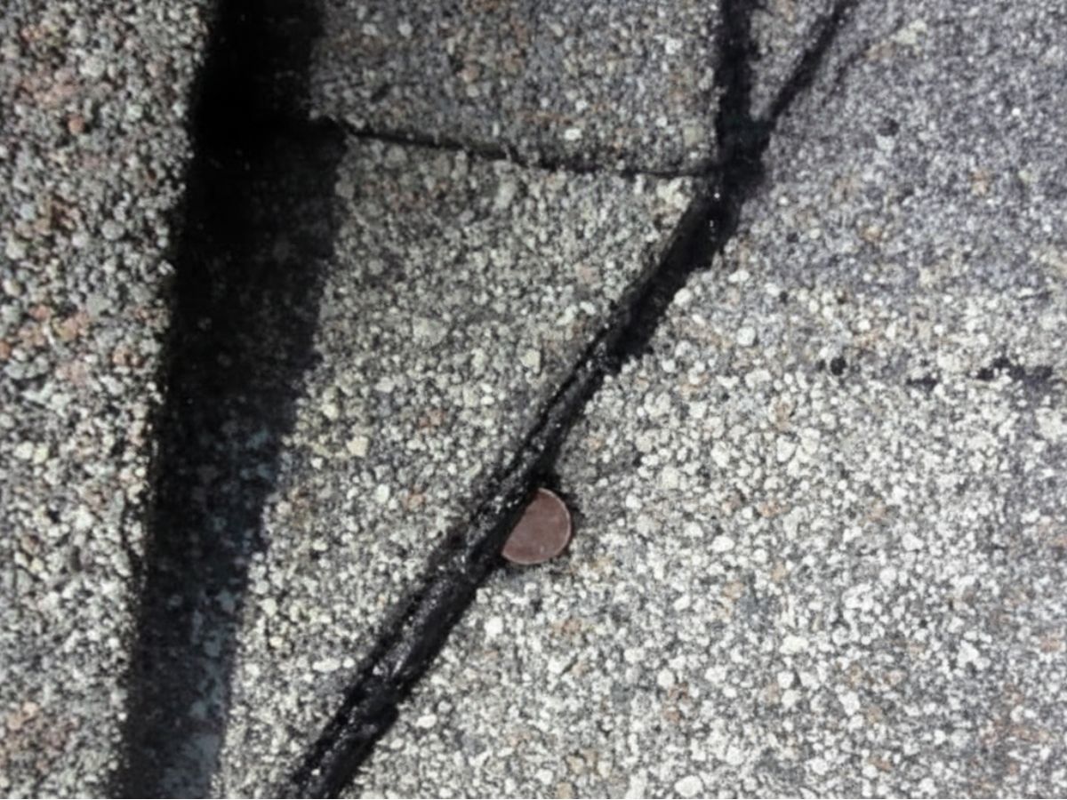 Exposed and protruding roofing nail through shingle seam, creating a potential leak point and indicating fastening failure