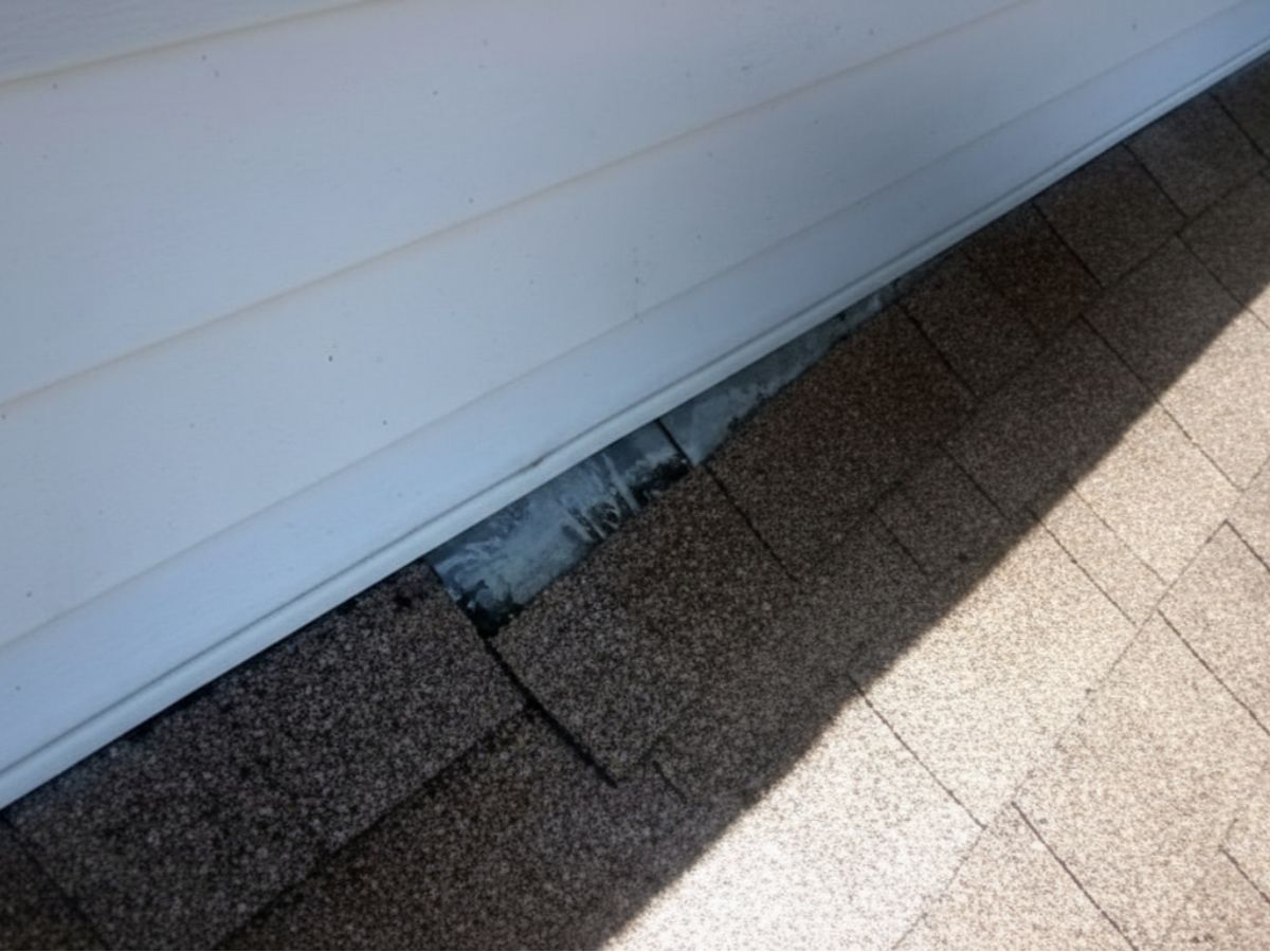 Improper or missing flashing at roof-to-wall intersection, exposing underlying metal and increasing risk of water intrusion