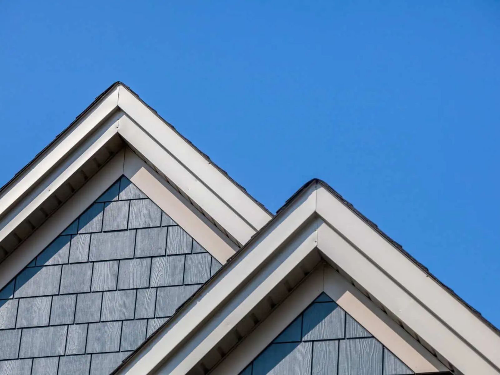 Residential roof gables with architectural shingles and fascia trim under a clear blue sky