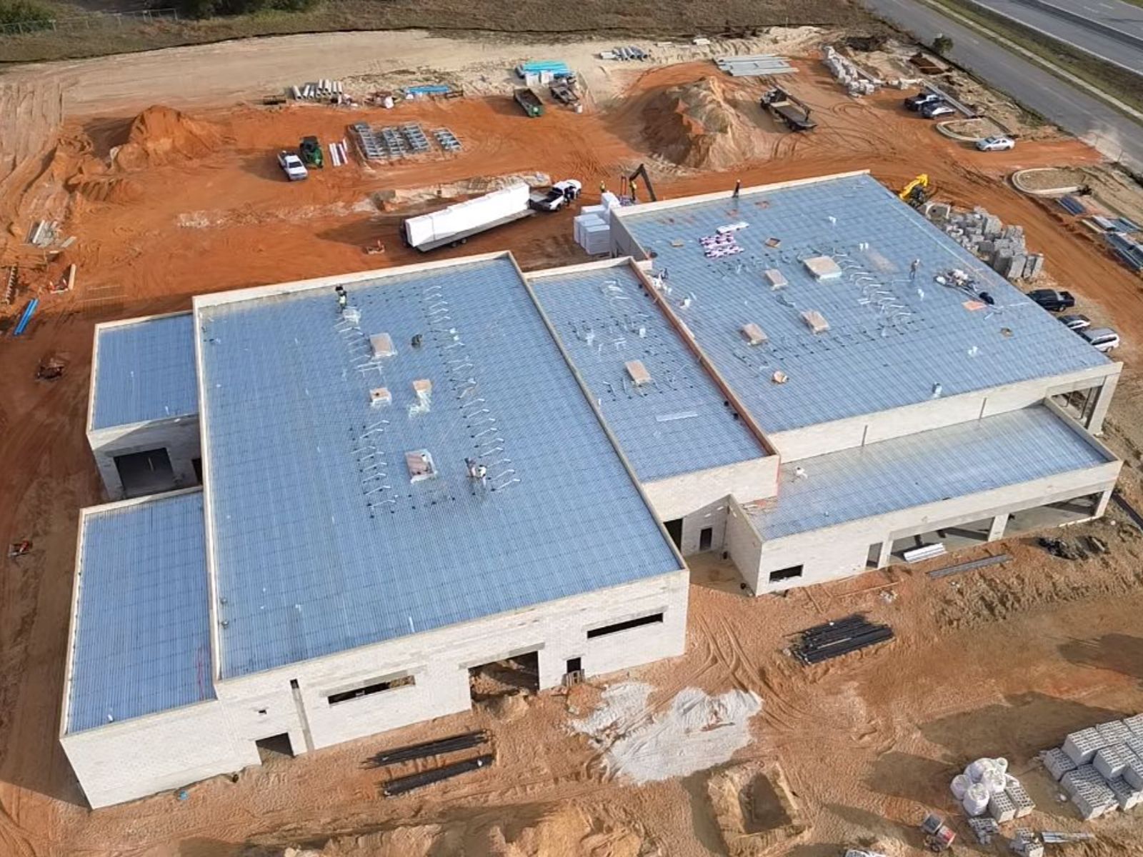 Aerial view of a large commercial building under construction with flat metal roof decking and surrounding construction equipment and materials