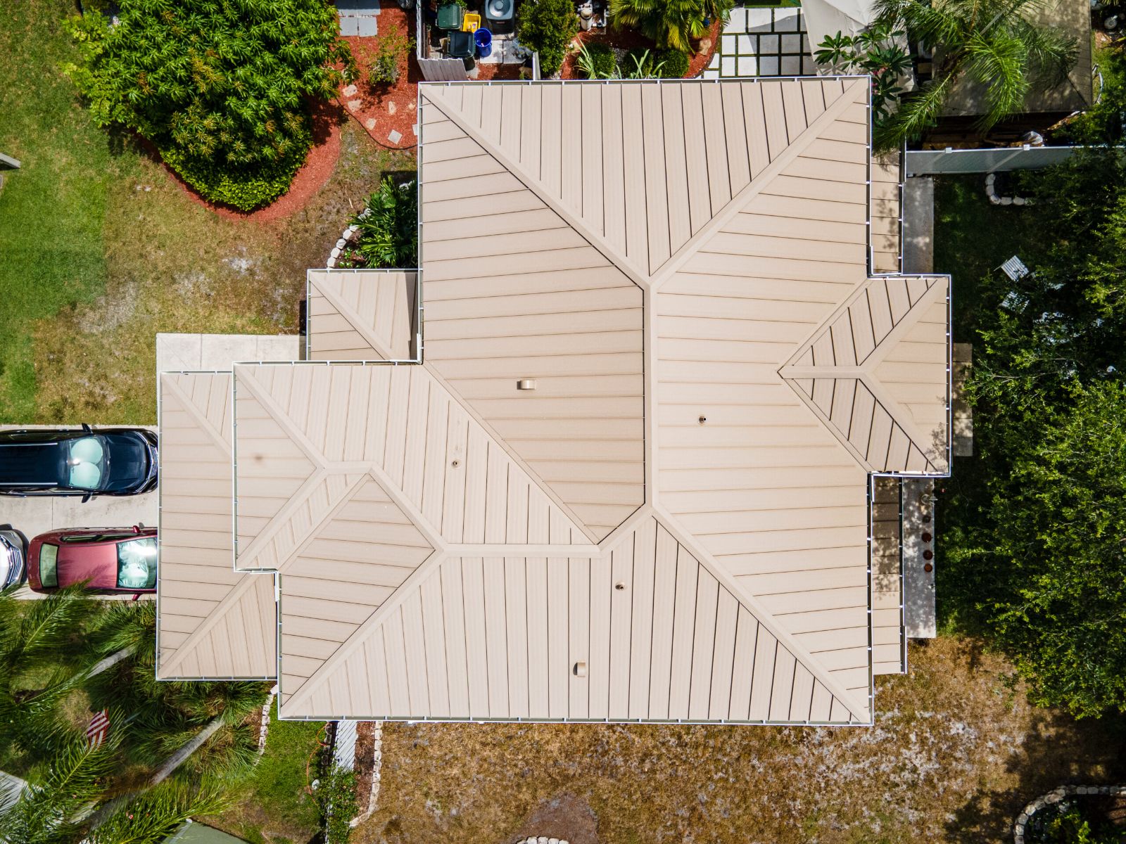 Aerial top-down view of a home with a tan standing seam metal roof and surrounding yard.