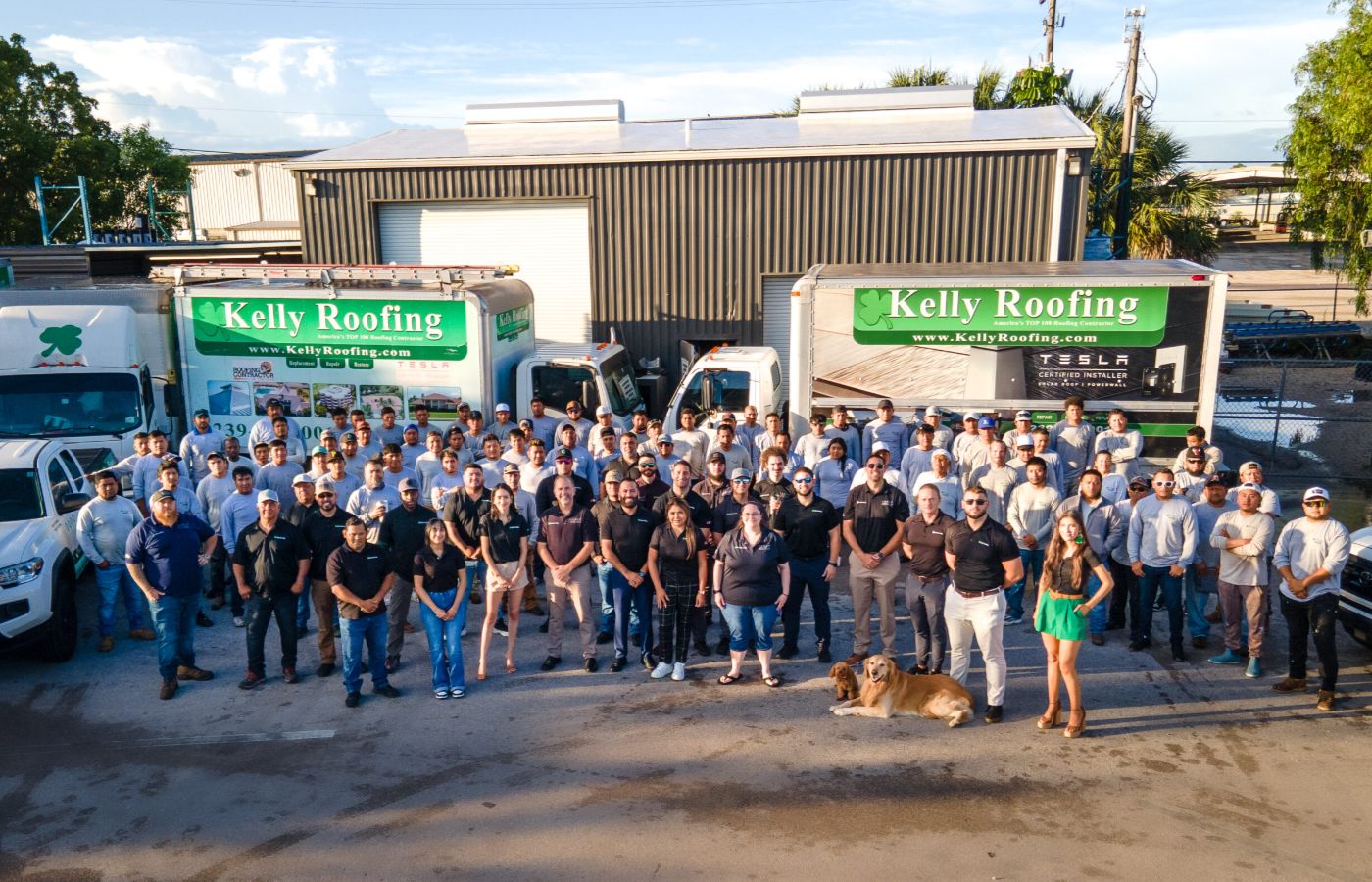 Kelly Roofing team group photo standing in front of company trucks and headquarters, showcasing staff and fleet.