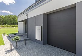 Modern home exterior with integrated solar battery storage system mounted on the wall beside a garage