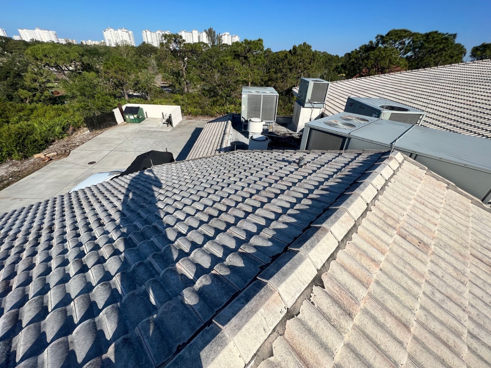 user-inserted Concrete tile roof with visible shadows, showing HVAC units on the rooftop and a clear blue sky in the background.