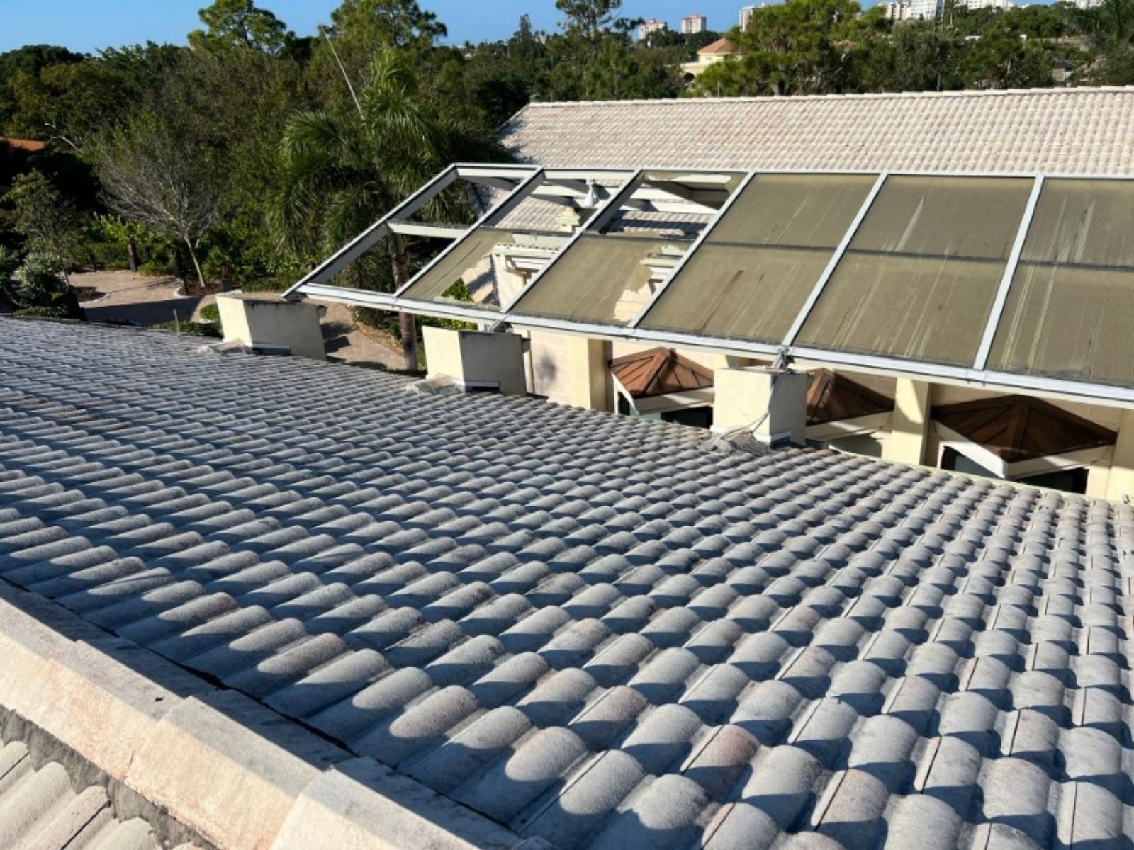 user-inserted Concrete tile roof with visible ridges, featuring a sunroom with mesh panels and a clear sky in the background.